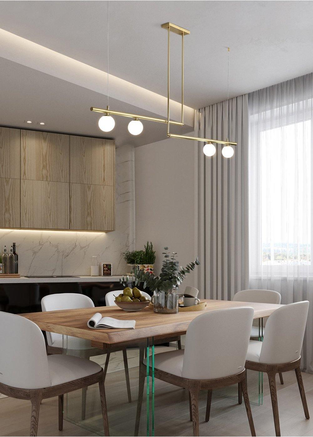 Clérachic gold pendant with four globes on two bars above a timber dining table, with white chairs and a long kitchen behind.