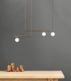 Clérachic gold pendant with three opal globes against a dark grey wall, above a pale wood table with small wooden figures.