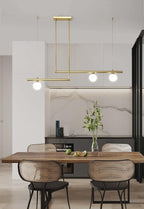 Clérachic gold pendant with three globes hung above a wooden dining table with woven chairs, with a marble wall behind.