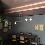 Clérachic gold pendant with three globes in a dark grey dining room, above a wooden table with cane-backed chairs.
