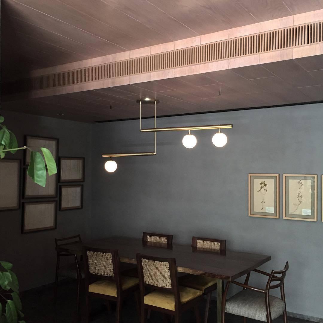 Clérachic gold pendant with three globes in a dark grey dining room, above a wooden table with cane-backed chairs.