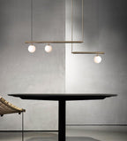 Clérachic gold pendant with three globes on offset bars, above a round black table against a concrete-effect wall.