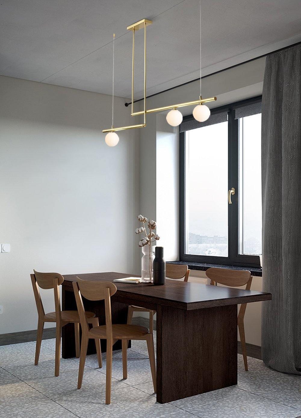 Clérachic gold pendant with three globes beside a large window, above a dark wooden dining table with tan chairs.