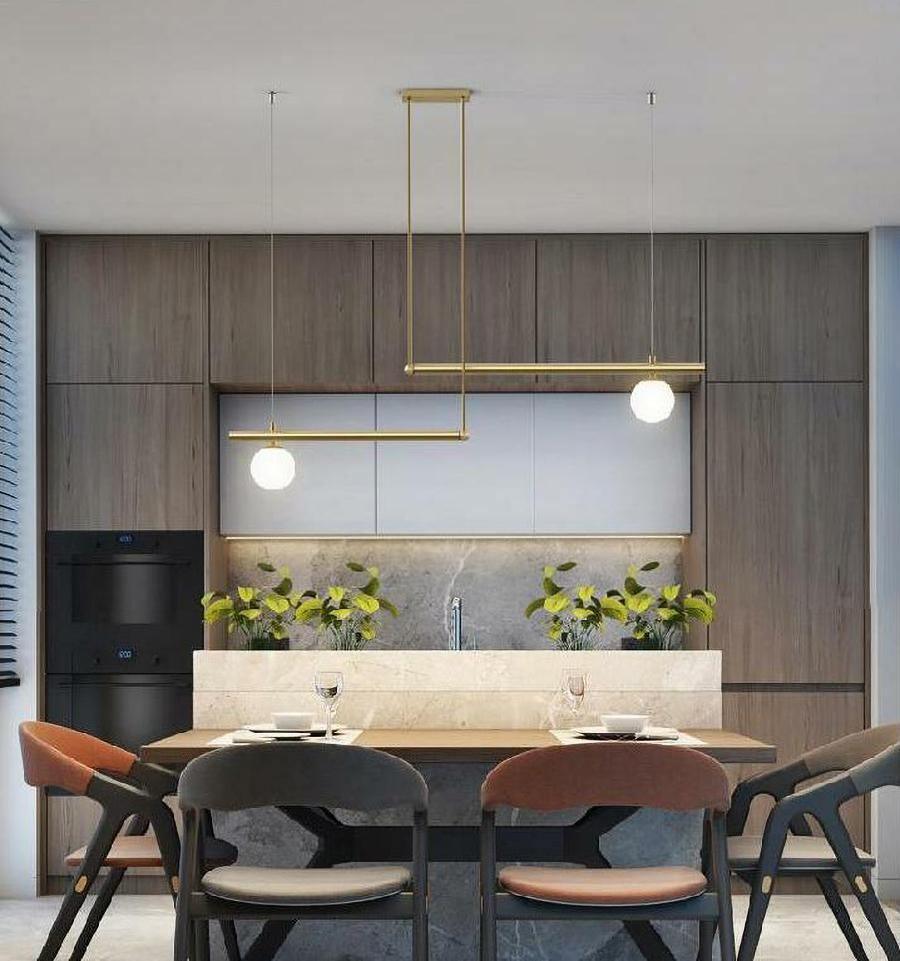 Clérachic gold pendant with two offset bars and two glowing globes in a dark timber kitchen, above a dining table.