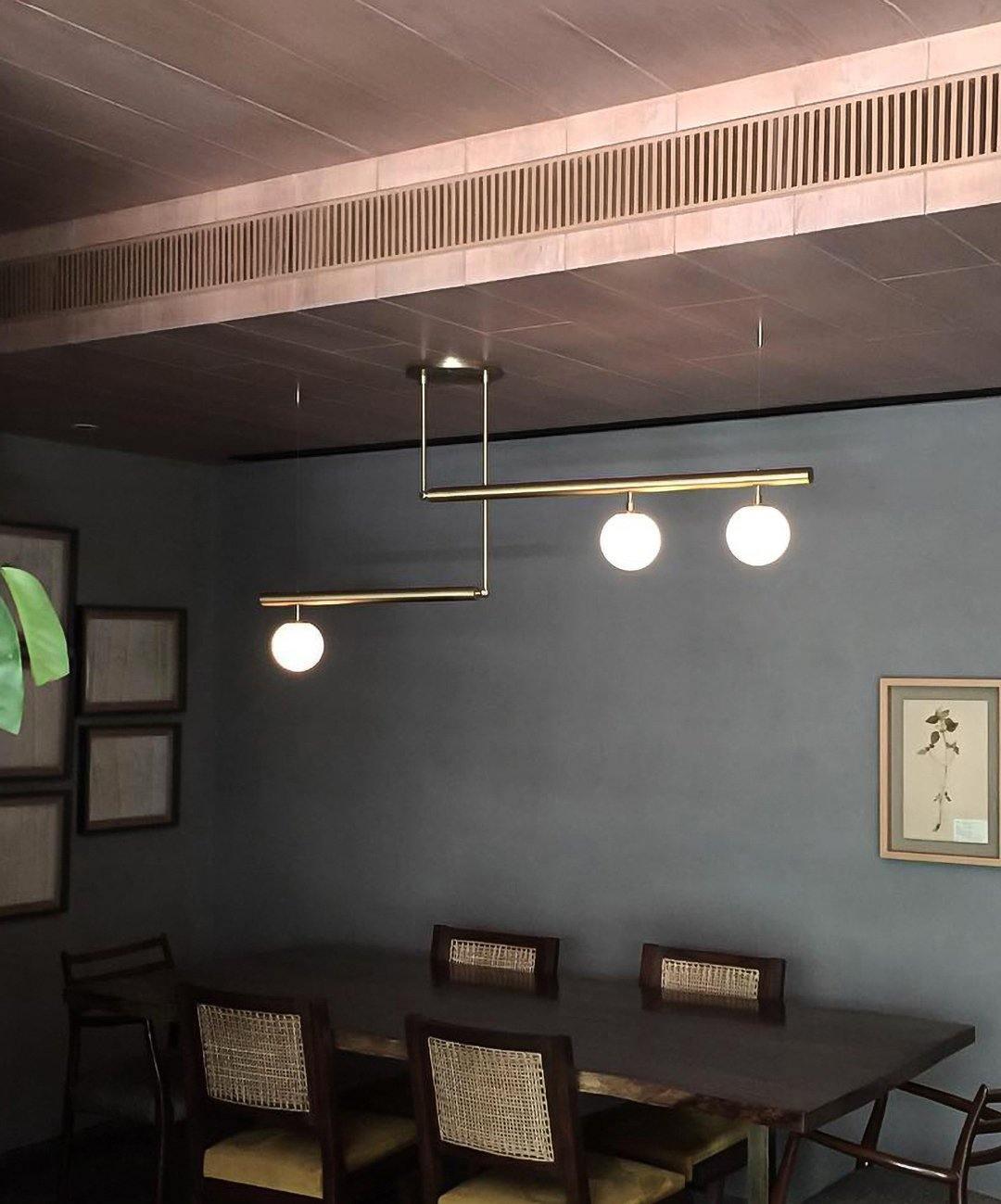 Clérachic gold pendant with three globes in a dark grey dining room, with framed botanical prints and woven chairs below.
