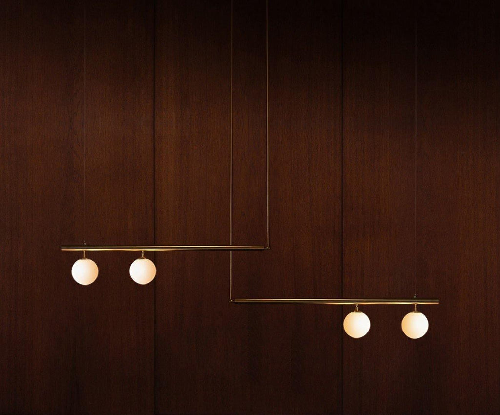 Clérachic pendant with two bars carrying four lit opal globes, hanging against a dark mahogany wall.