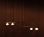 Clérachic pendant with two bars carrying four lit opal globes, hanging against a dark mahogany wall.