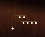 Larger Clérachic pendant with three bars carrying seven lit opal globes, hanging against a dark mahogany wall.