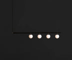 Black Clérachic pendant bar with four opal globes, lit and hanging against a near-black background.