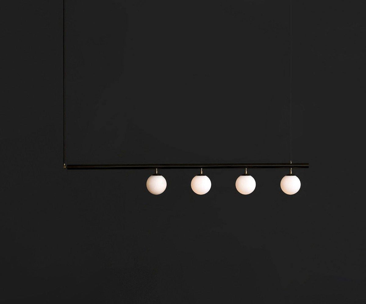 Black Clérachic pendant bar with four opal globes, lit and hanging against a near-black background.