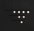 Black Clérachic pendant with three stepped bars carrying seven lit opal globes, against a near-black background.