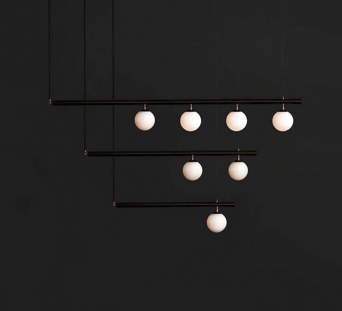 Black Clérachic pendant with three stepped bars carrying seven lit opal globes, against a near-black background.