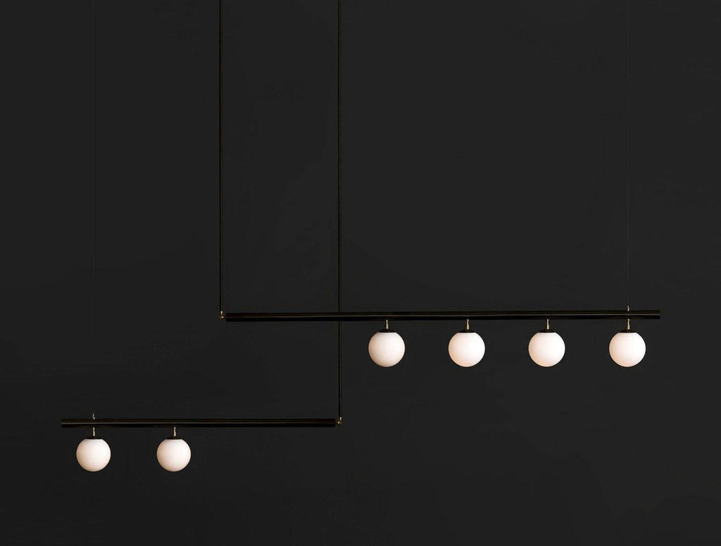 Black Clérachic pendant with two offset bars and six lit opal globes, hanging against a near-black background.