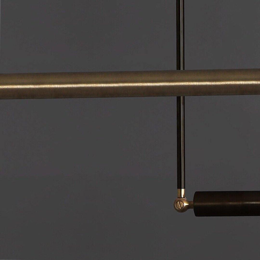 Close view of the darker brass bar and the black rod and swivel joint of this Clérachic pendant, on a charcoal background.