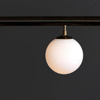 Close view of an opal glass globe and its brass cap hanging from a dark bar on this Clérachic pendant.