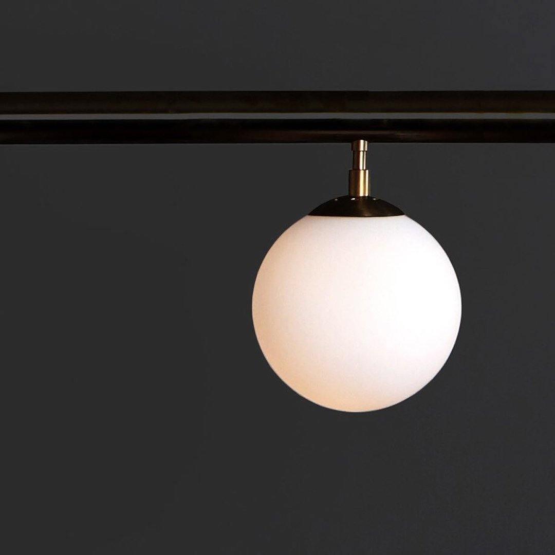 Close view of an opal glass globe and its brass cap hanging from a dark bar on this Clérachic pendant.