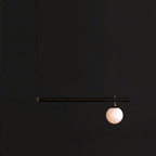 Single-globe black Clérachic pendant with one long rod and a short bar, lit against a near-black background.