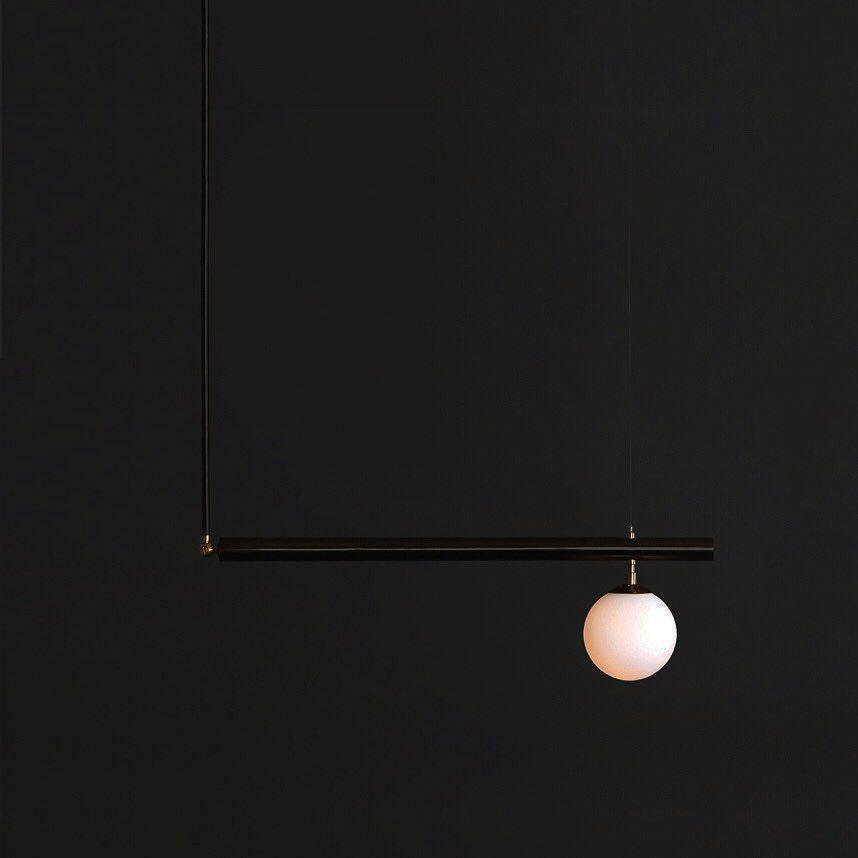 Single-globe black Clérachic pendant with one long rod and a short bar, lit against a near-black background.
