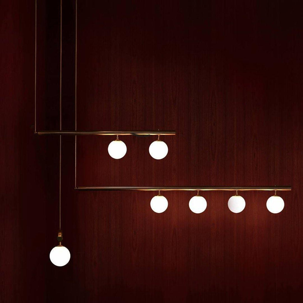 Clérachic gold pendant with three bars, six lit globes and one single drop globe, against a deep red timber wall.