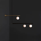Clérachic pendant with a wall-fixed brass arm and a black bar, three lit globes in all, against a dark grey wall.