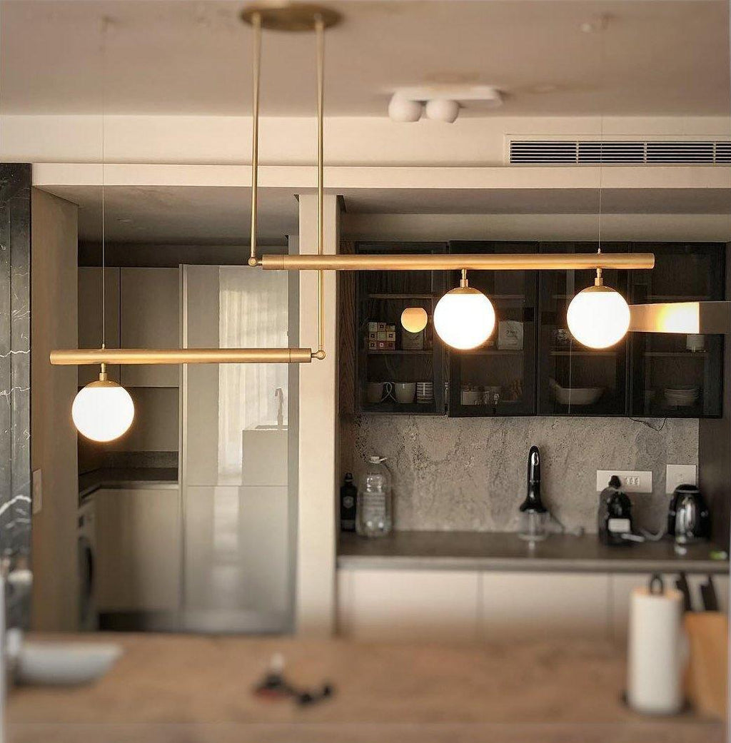 Clérachic gold pendant with three globes hung in a home kitchen with dark glazed cabinets and a stone splashback.