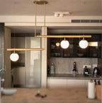 Clérachic gold pendant with three globes hung in a home kitchen with dark glazed cabinets and a stone splashback.