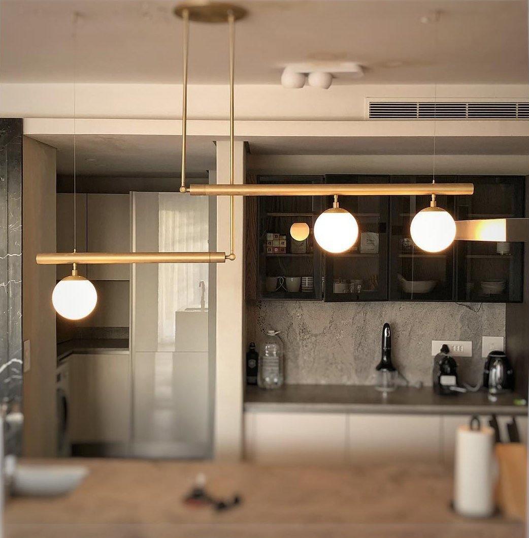 Clérachic gold pendant with three globes hung in a home kitchen with dark glazed cabinets and a stone splashback.