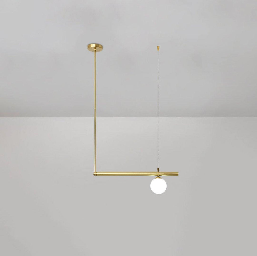 Single-globe Clérachic pendant hung from a round gold ceiling cap, with a gold rod and a short bar, on a pale grey wall.