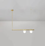 Two-globe Clérachic gold pendant hung from a round ceiling cap, with a gold rod and a long bar, on a pale grey wall.