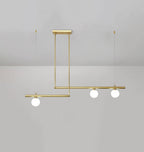 Clérachic gold pendant with three globes on two offset bars, hung from a rectangular plate on a pale grey wall.
