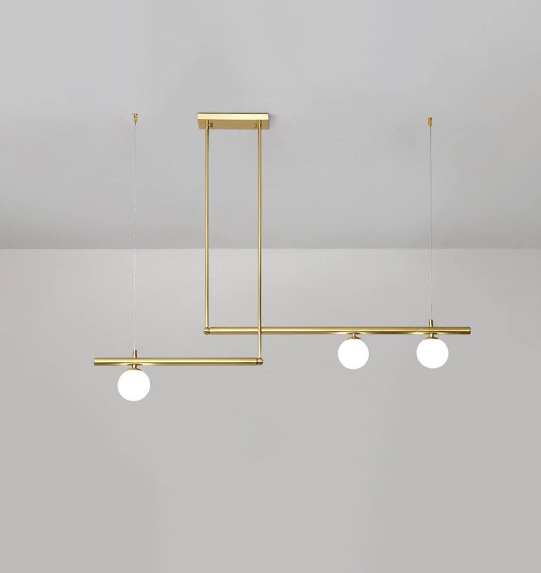 Clérachic gold pendant with three globes on two offset bars, hung from a rectangular plate on a pale grey wall.