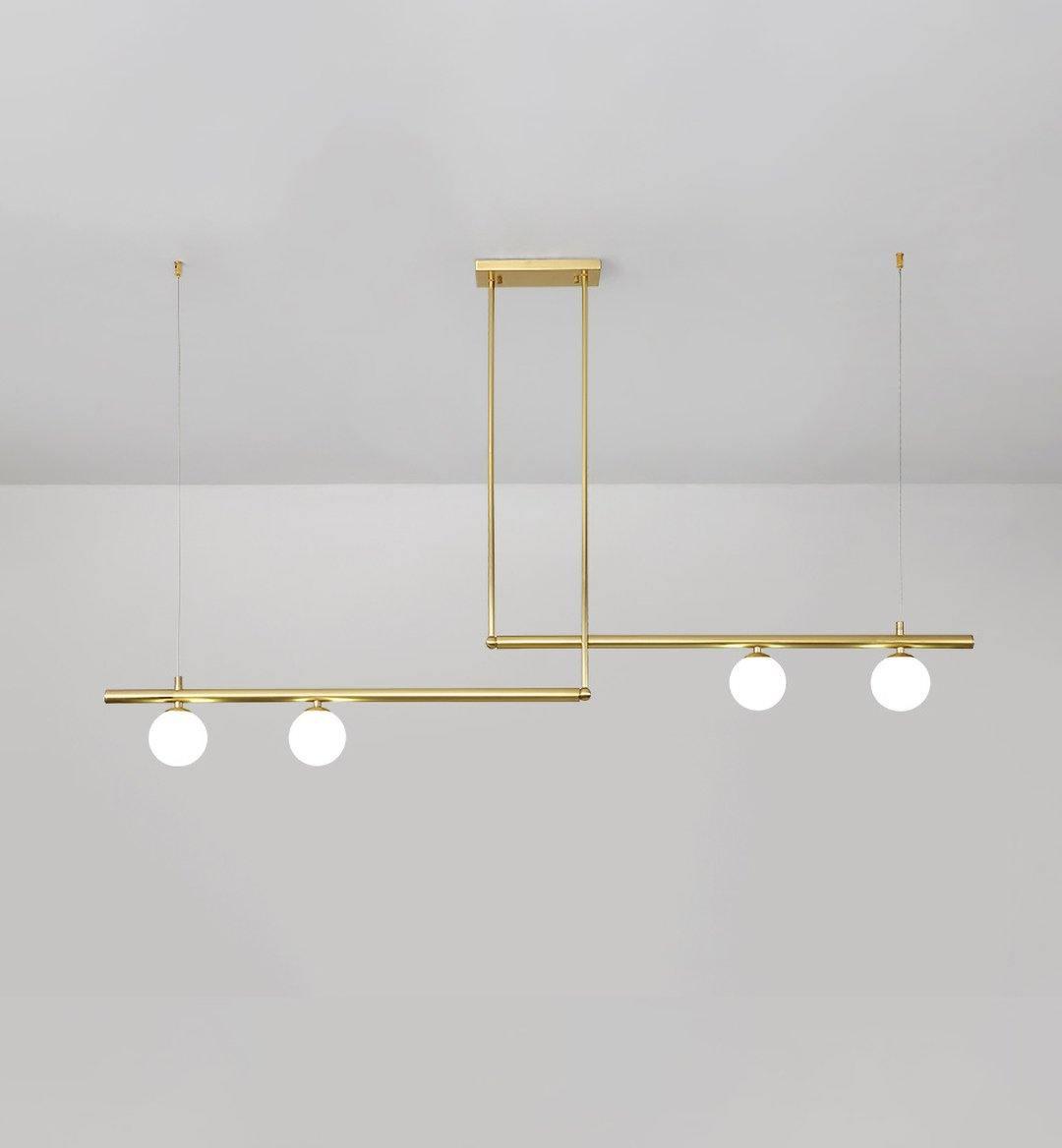 Clérachic gold pendant with four opal globes on two offset bars, hung from a rectangular plate on a pale grey wall.
