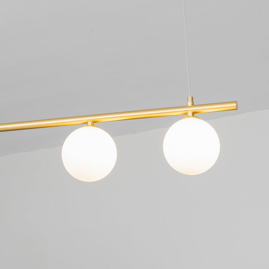 Close view of two opal glass globes under a gold bar on this Clérachic pendant, against a pale grey ceiling.