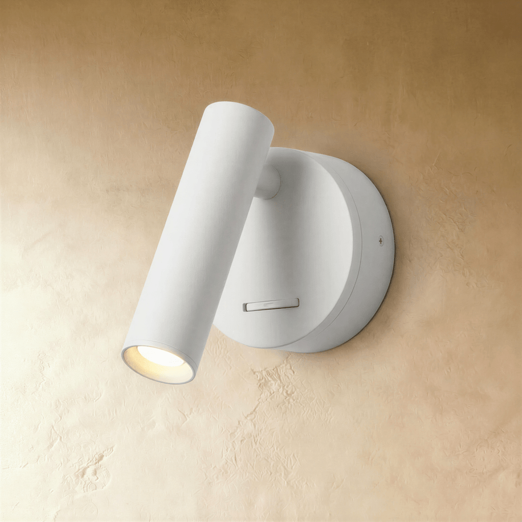 Clérachic white wall reading light, a slim cylinder head pivoting off a round backplate and lit warm on a limewash wall.