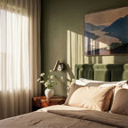 Clérachic wall reading light above a burr-wood bedside table in a green-walled bedroom, beside a velvet headboard.
