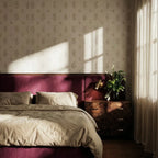 Clérachic brass wall reading light mounted above a burr-wood bedside chest, beside a plum headboard and a vase of greenery.