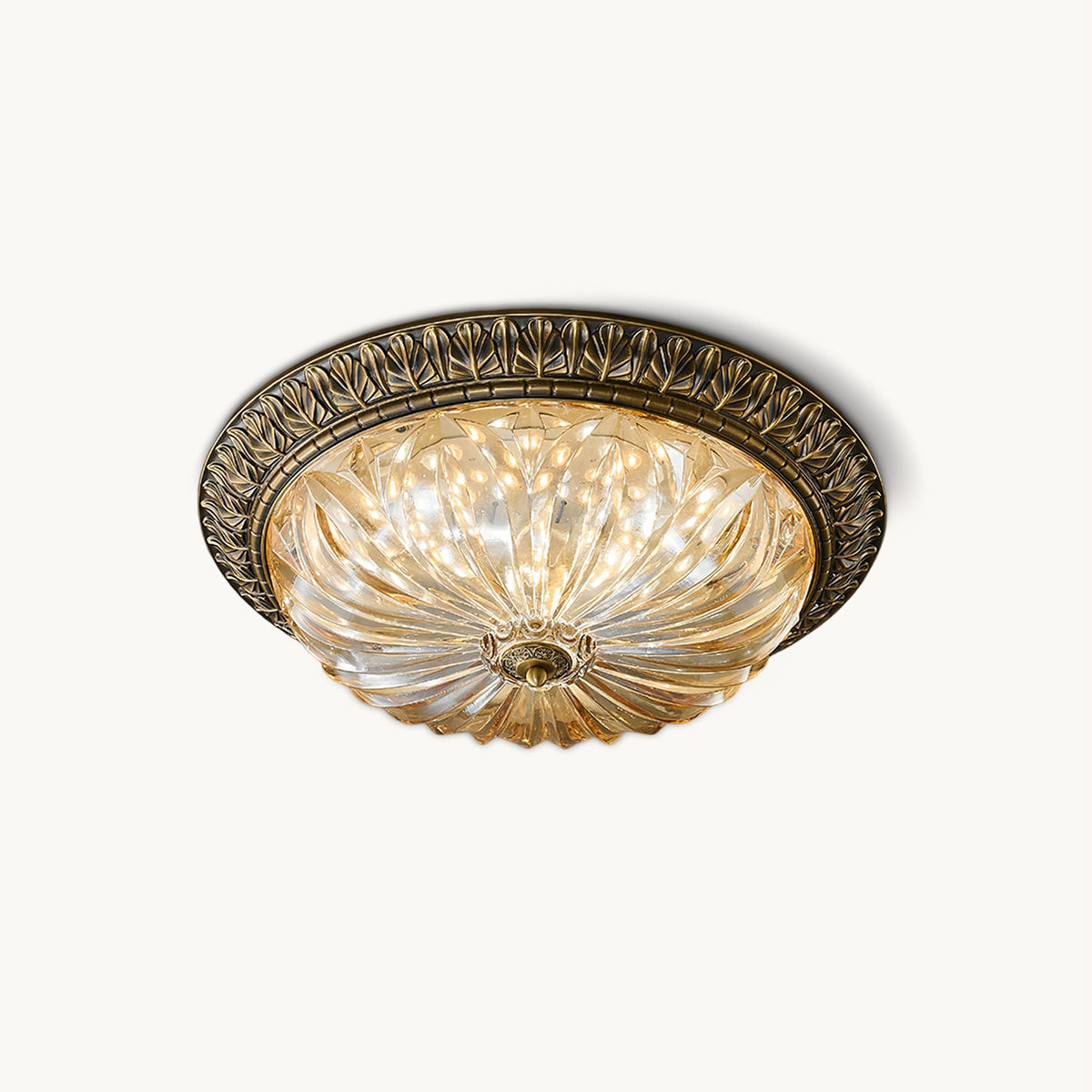 This Clérachic flush-mount ceiling light on a plain white backdrop, a lit amber pleated glass bowl in a leaf-patterned antique brass rim.