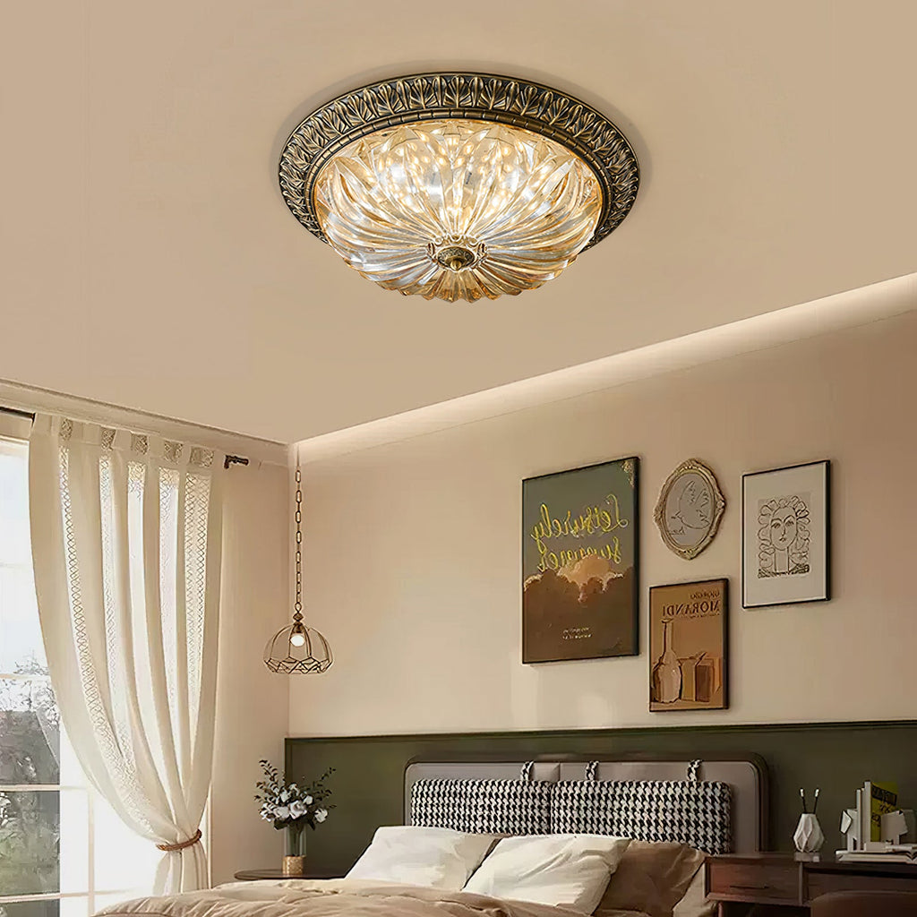 Lit amber glass of this Clérachic ceiling light above a bed with a houndstooth headboard, a green wall and framed prints.