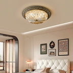 A Clérachic flush ceiling light glowing in a cream bedroom with a cove-lit ceiling and a quilted white headboard.