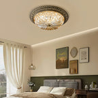This Clérachic amber glass ceiling light centred above a bedroom with a houndstooth headboard, linen curtains and a pendant light.