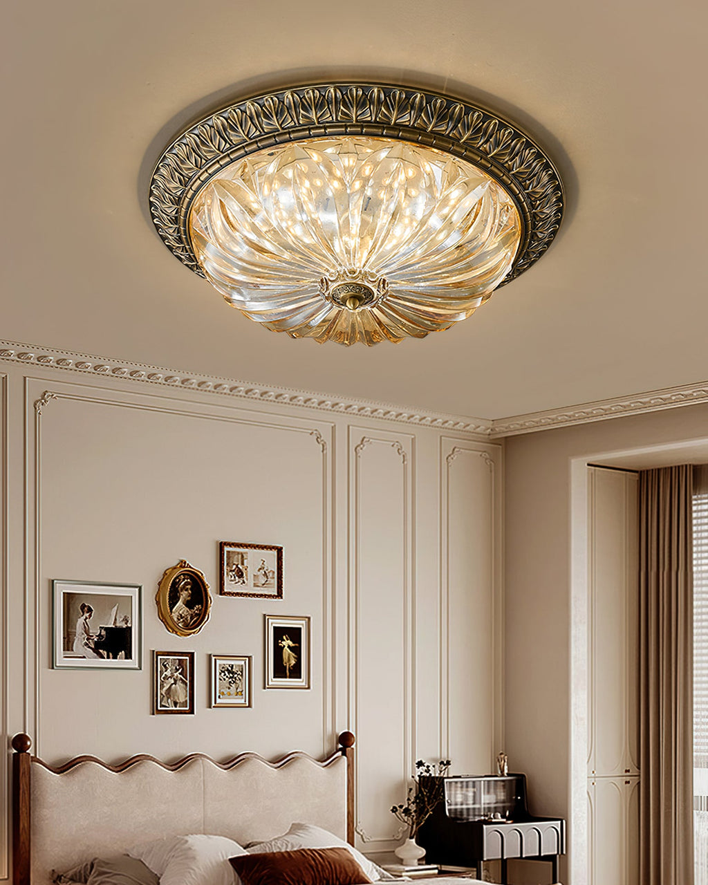 A Clérachic ceiling light in a tall panelled room, the amber glass lit above a scalloped headboard and a gallery of small frames.