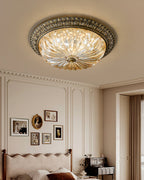 A Clérachic ceiling light in a tall panelled room, the amber glass lit above a scalloped headboard and a gallery of small frames.