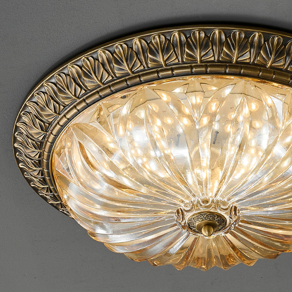 Close view of the leaf-patterned antique brass rim and ribbed amber glass of this Clérachic ceiling light on a dark grey ceiling.