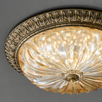 Close view of the leaf-patterned antique brass rim and ribbed amber glass of this Clérachic ceiling light on a dark grey ceiling.