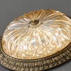 Angled close view of the ribbed amber glass bowl of this Clérachic ceiling light, lit, with its brass rim and centre boss.