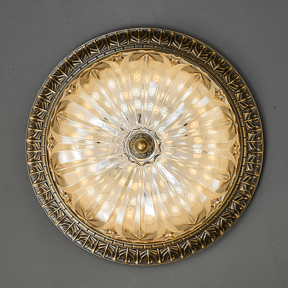 Looking straight up at this Clérachic ceiling light, the round amber glass lit inside a leaf-patterned brass rim.