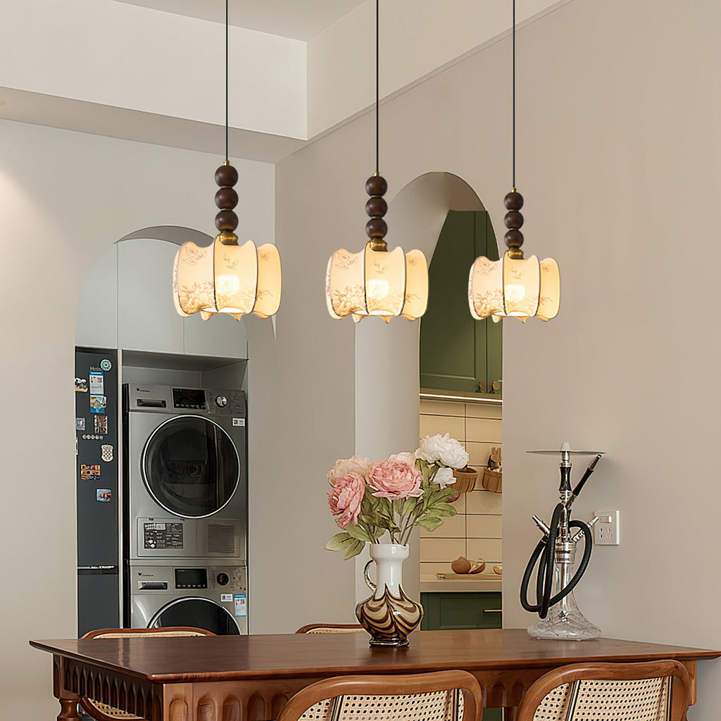 Three Clérachic pendants with gathered cream shades and walnut beads hang in a row above a wooden dining table by an arched doorway.