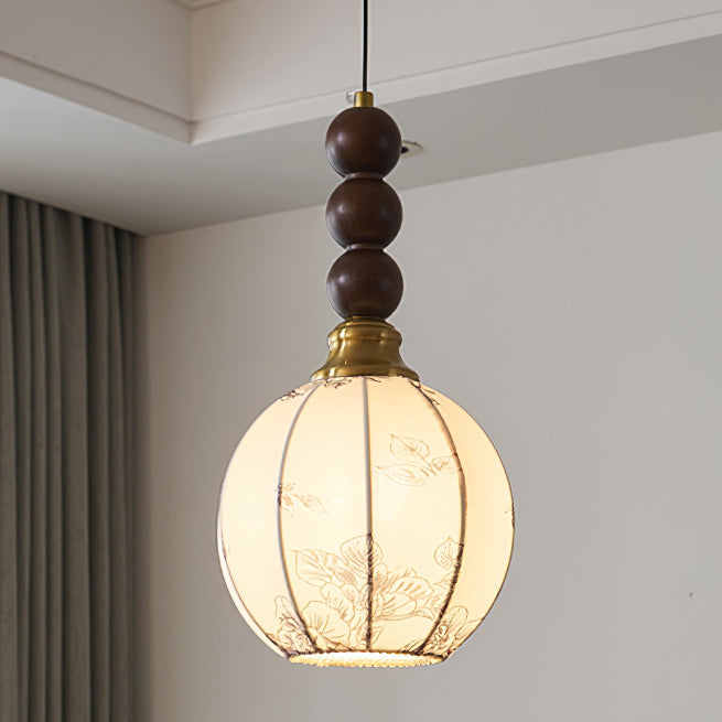 Close view of the round cream shade, brass cap and three stacked walnut beads of this Clérachic pendant, lit warm.