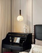 This Clérachic round-shaded pendant hangs over a black desk and an angel figure, beside a carved dark headboard and a cream curtain.