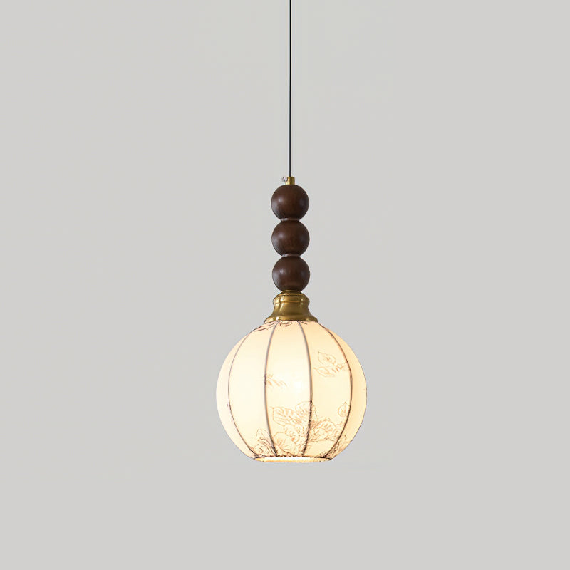 A Clérachic pendant with a round cream shade, lit warm, a brass cap and three walnut beads, on a light grey background.